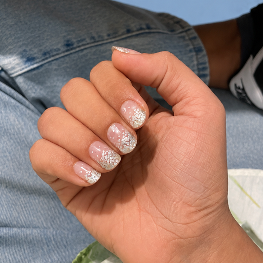 Hand with glittery silver namora nail wraps against a blurred green background