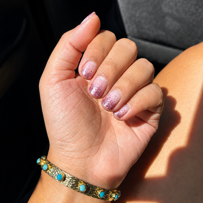 Hand with pink glittery nail wraps wearing a bracelet on a dark background