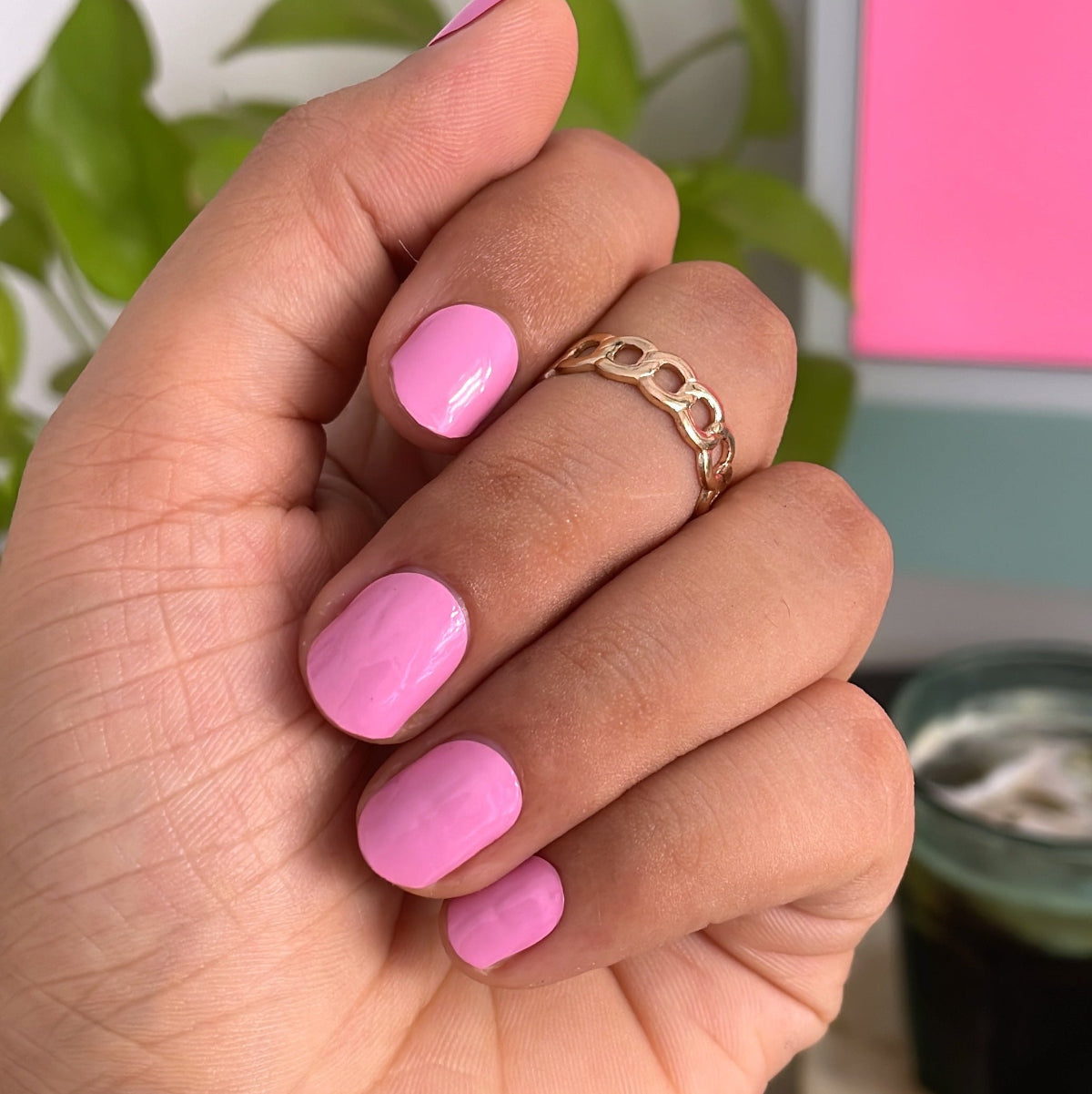 Hand with pink nails and a gold ring, blurred background